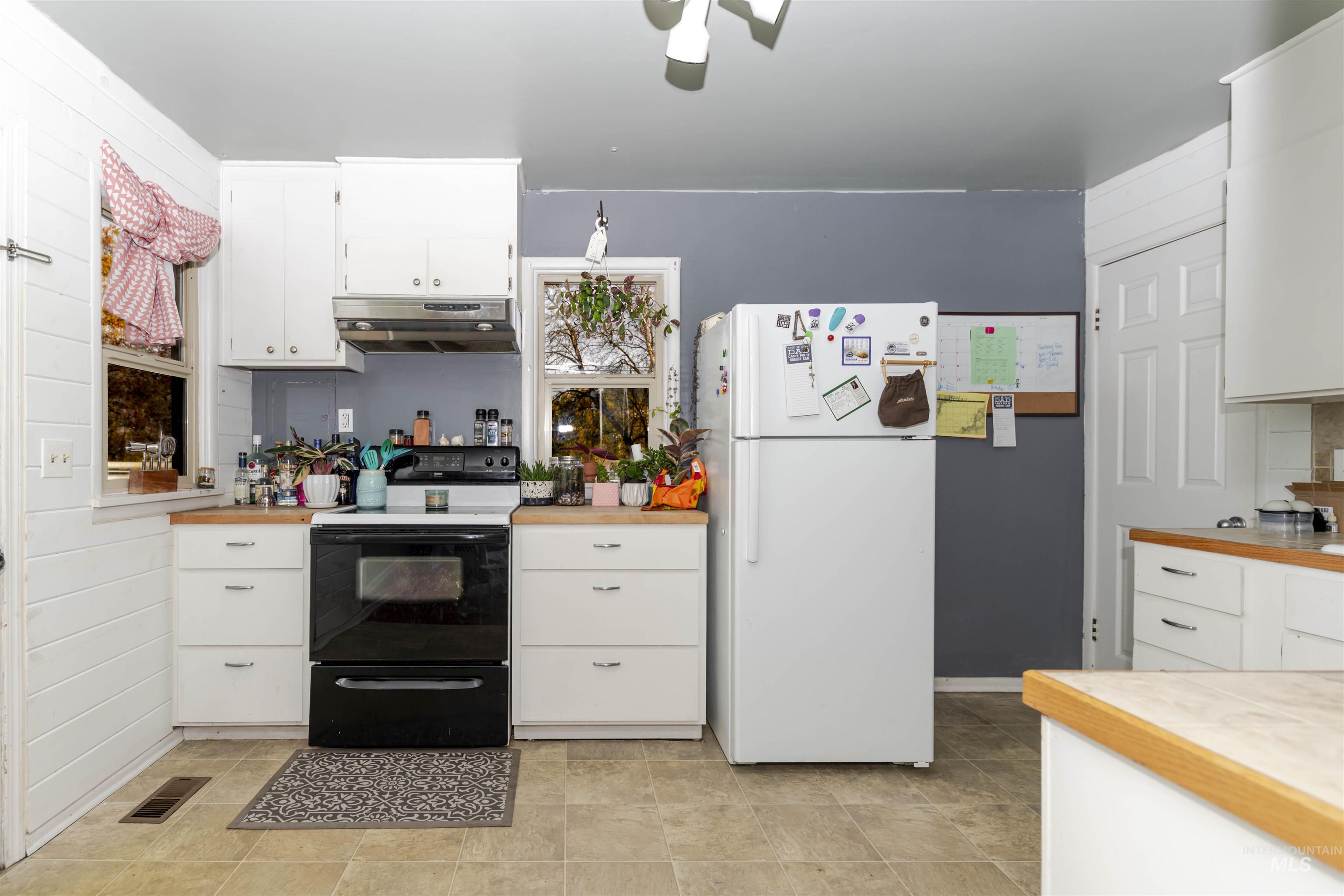 Kitchen featuring freestanding refrigerator, black / electric stove, white cabinetry, and light countertops