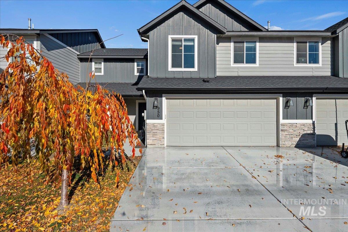 View of front of house with stone siding, driveway, board and batten siding, a garage, and a shingled roof