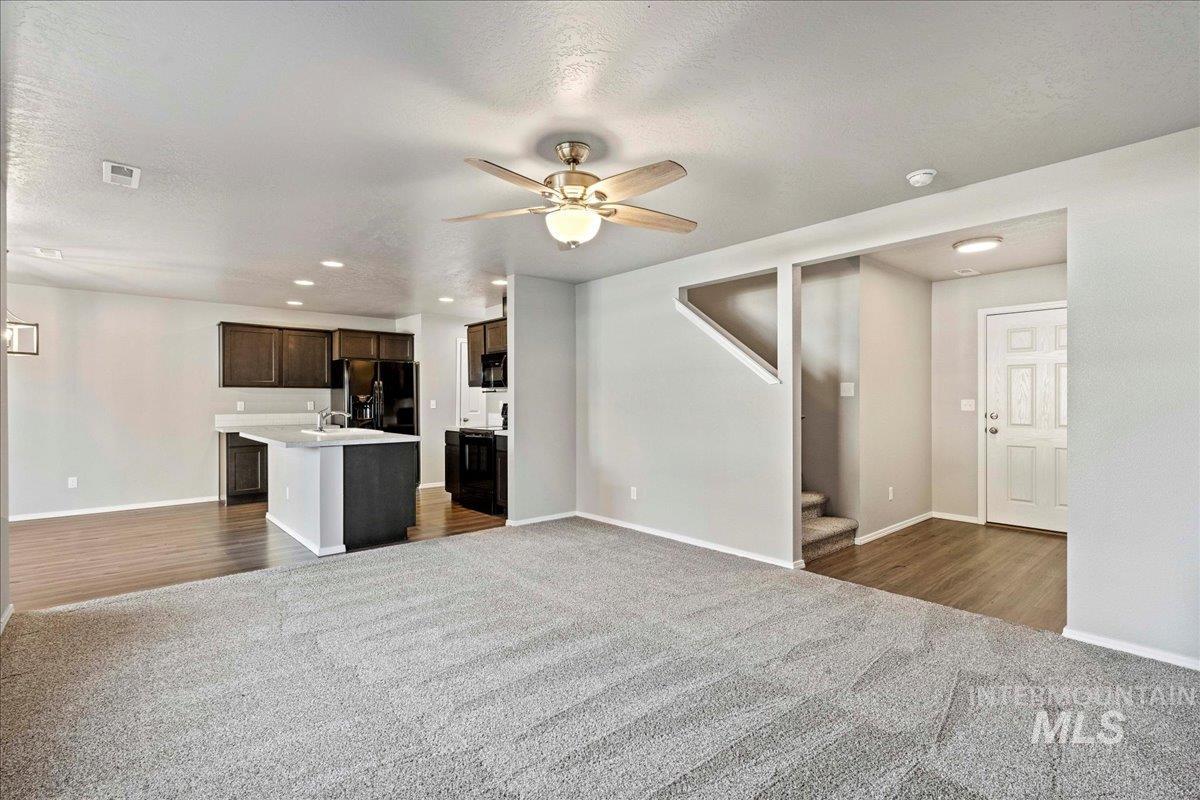 Unfurnished living room featuring dark colored carpet, a textured ceiling, recessed lighting, a ceiling fan, and stairway