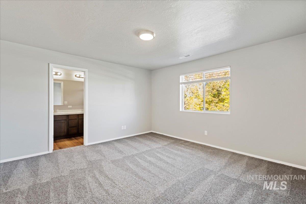 Unfurnished bedroom with light colored carpet, a textured ceiling, and connected bathroom