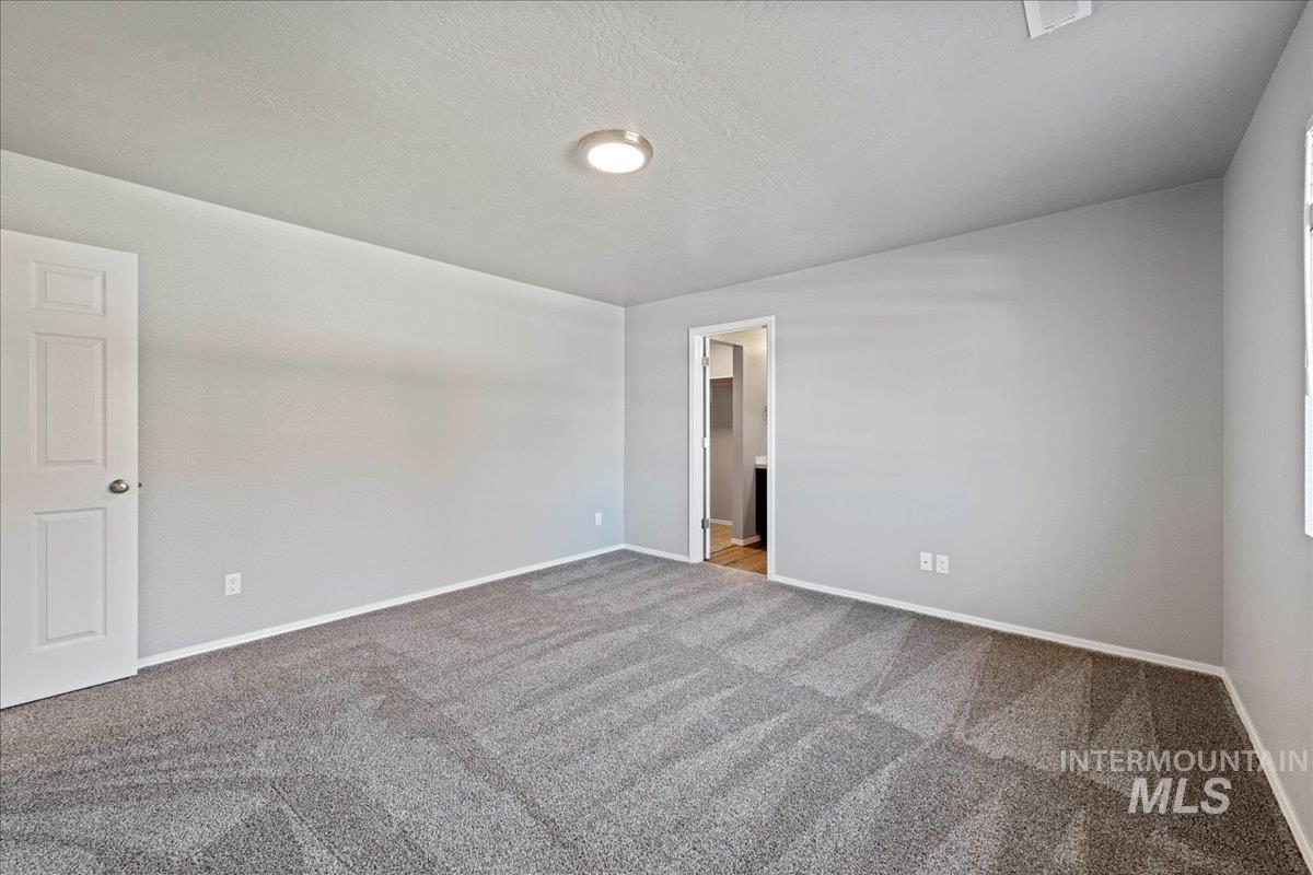 Carpeted spare room featuring a textured ceiling and baseboards
