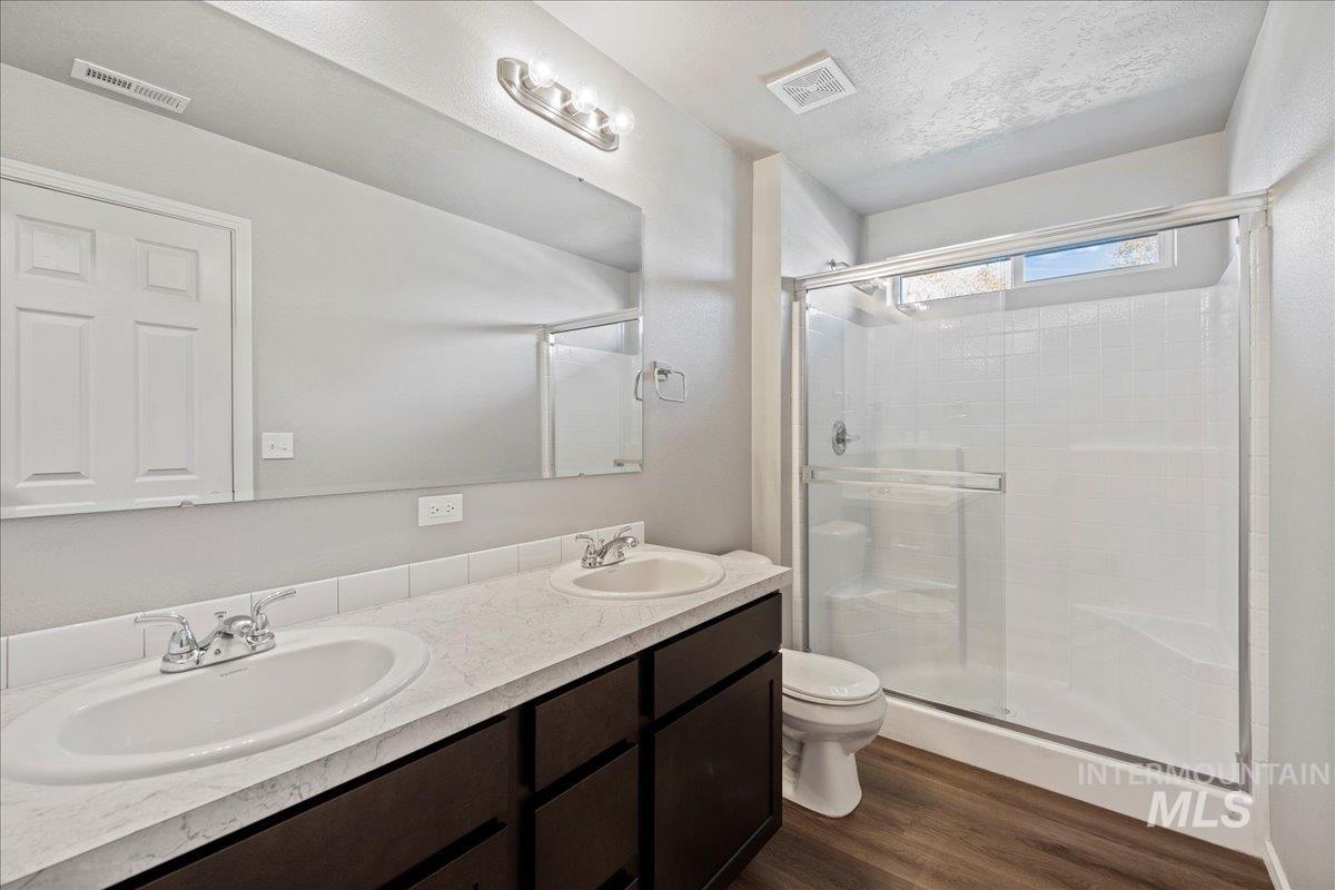 Full bath with dark wood-style flooring, double vanity, and a shower stall