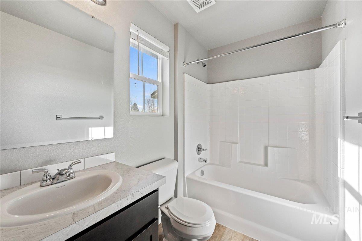 Bathroom featuring vanity,  shower combination, a textured wall, and light wood-style flooring