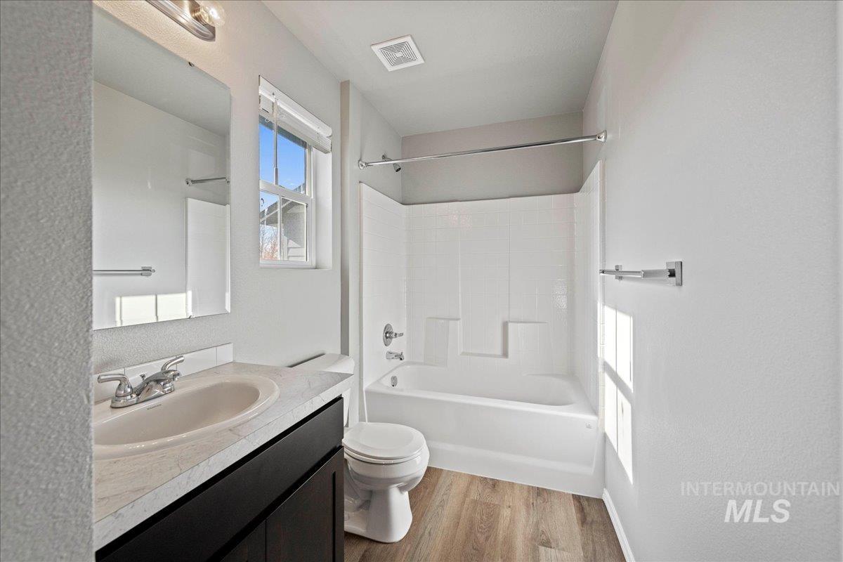 Full bath with washtub / shower combination, vanity, light wood-style floors, and a textured wall