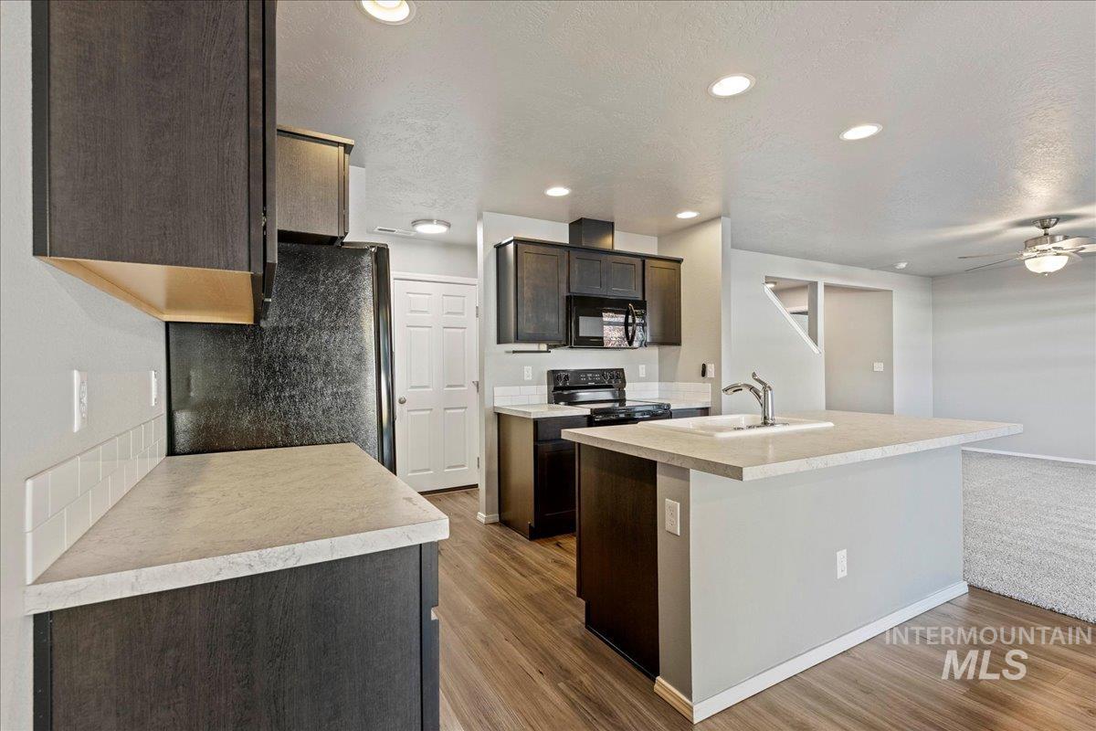 Kitchen featuring light countertops, black appliances, recessed lighting, dark brown cabinets, and an island with sink