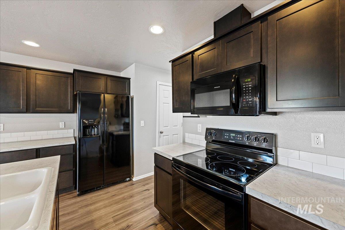 Kitchen with dark brown cabinetry, black appliances, light wood-style flooring, light countertops, and recessed lighting