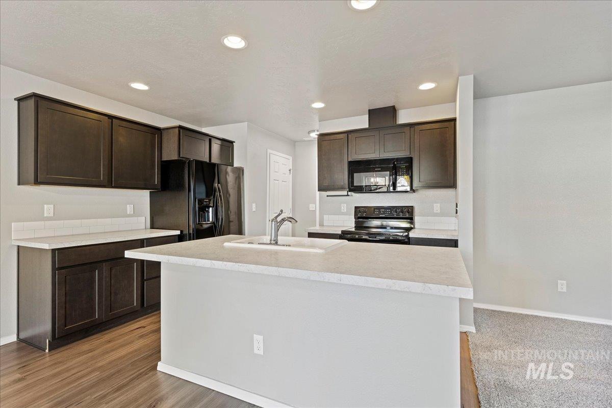 Kitchen featuring light countertops, dark brown cabinets, black appliances, a center island with sink, and recessed lighting