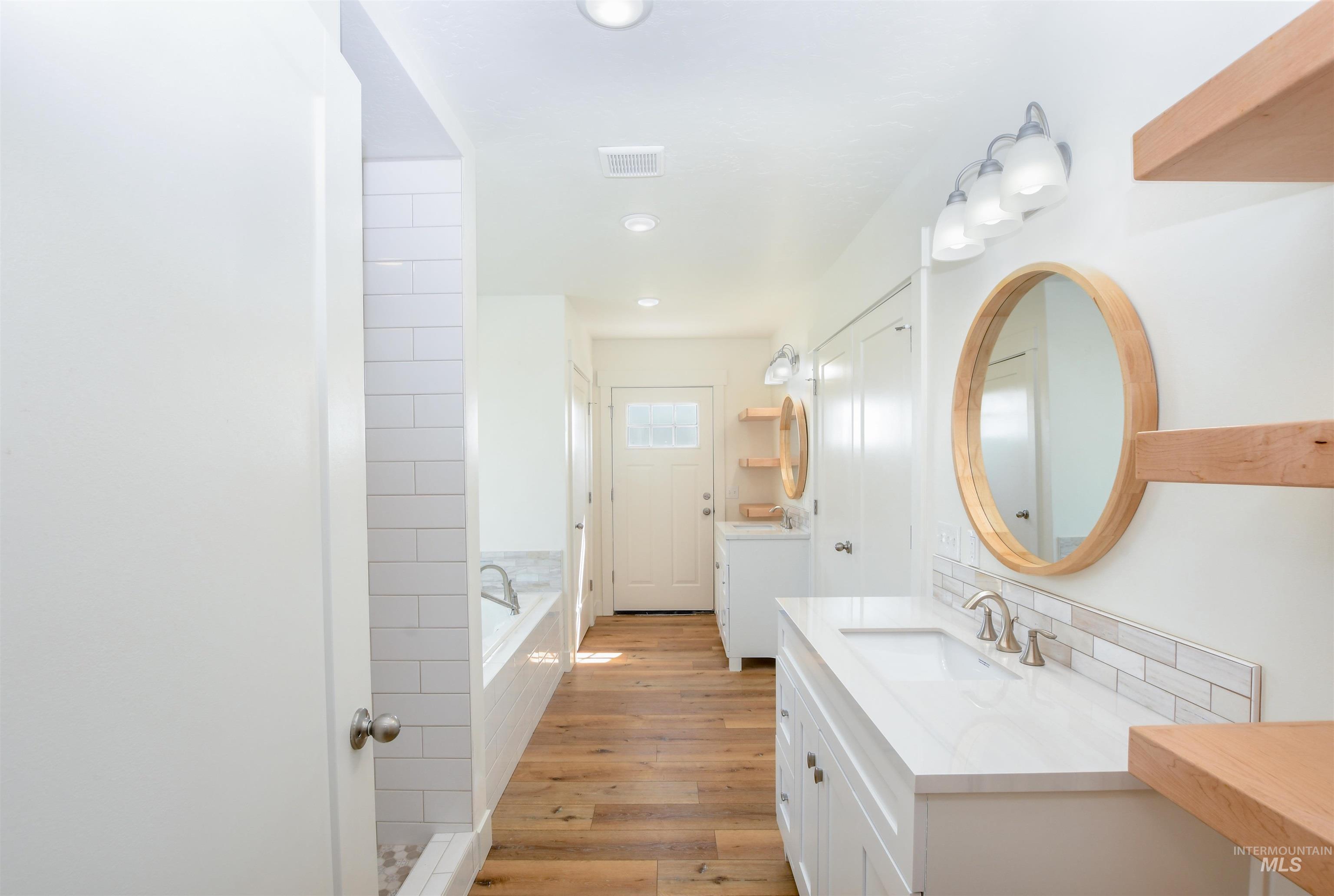 Bathroom featuring light wood-style flooring, two vanities, a bath, and recessed lighting