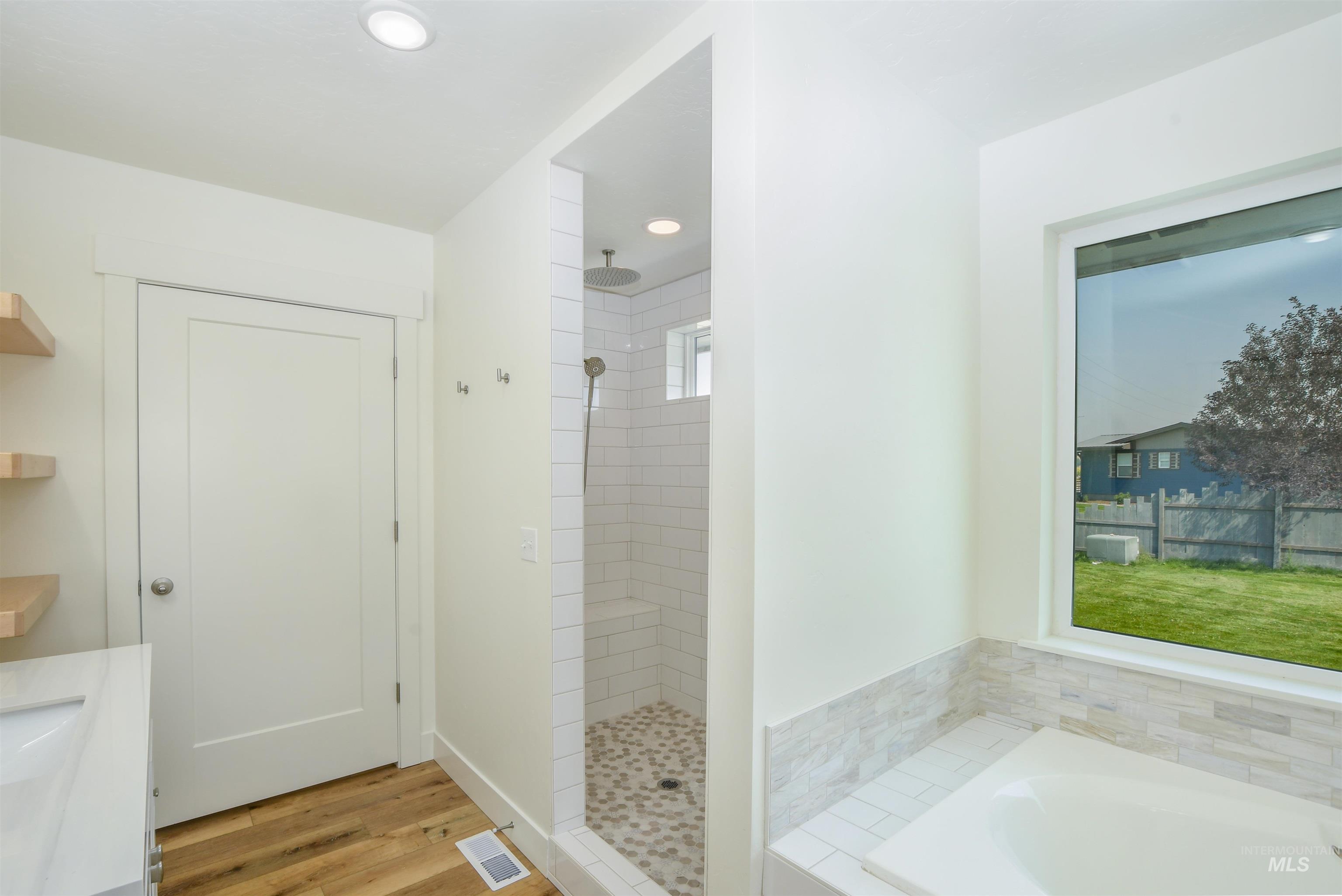 Bathroom featuring a garden tub, a tile shower, light wood-type flooring, recessed lighting, and double vanity