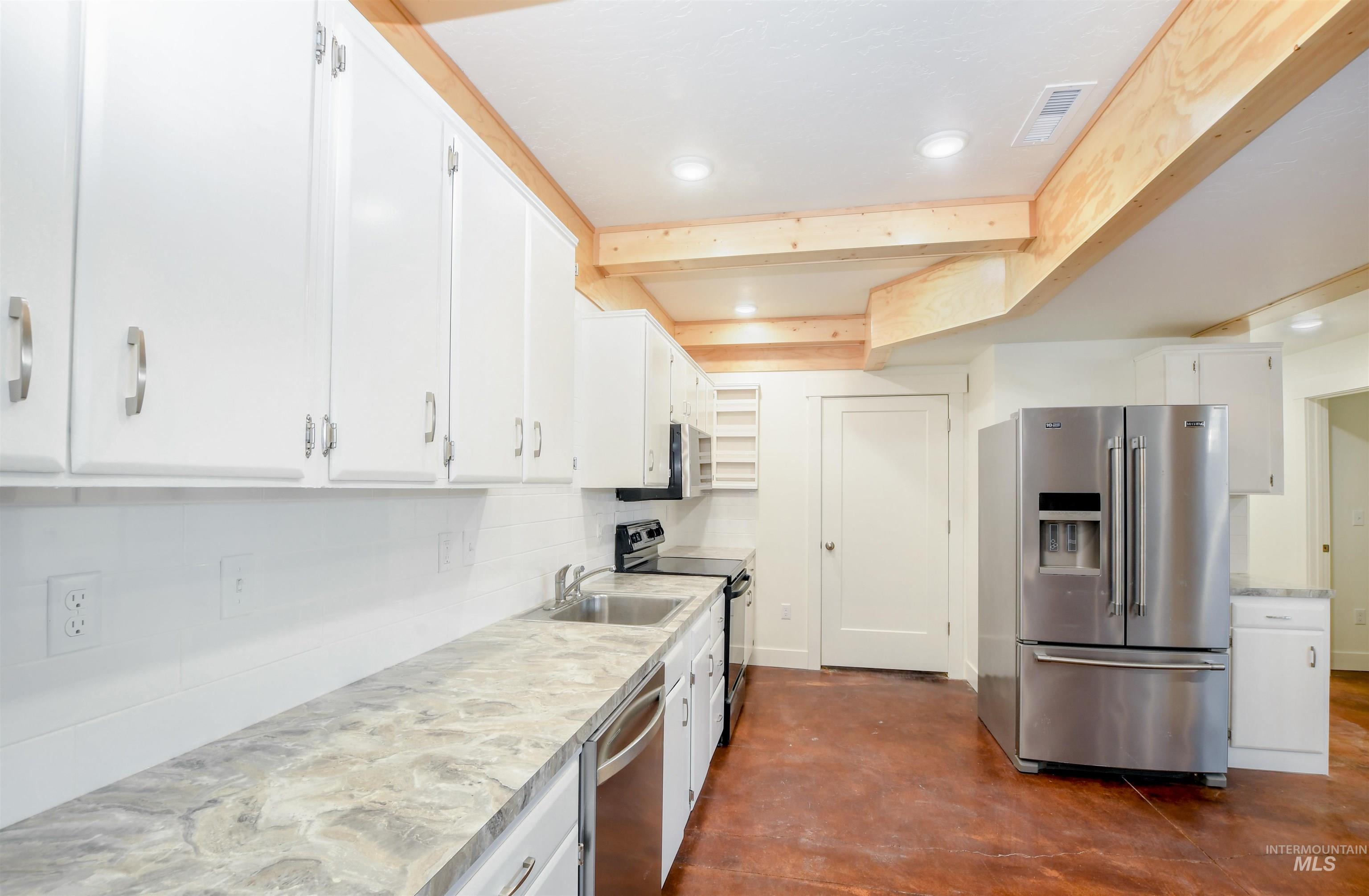 Kitchen with appliances with stainless steel finishes, white cabinets, light countertops, concrete flooring, and recessed lighting