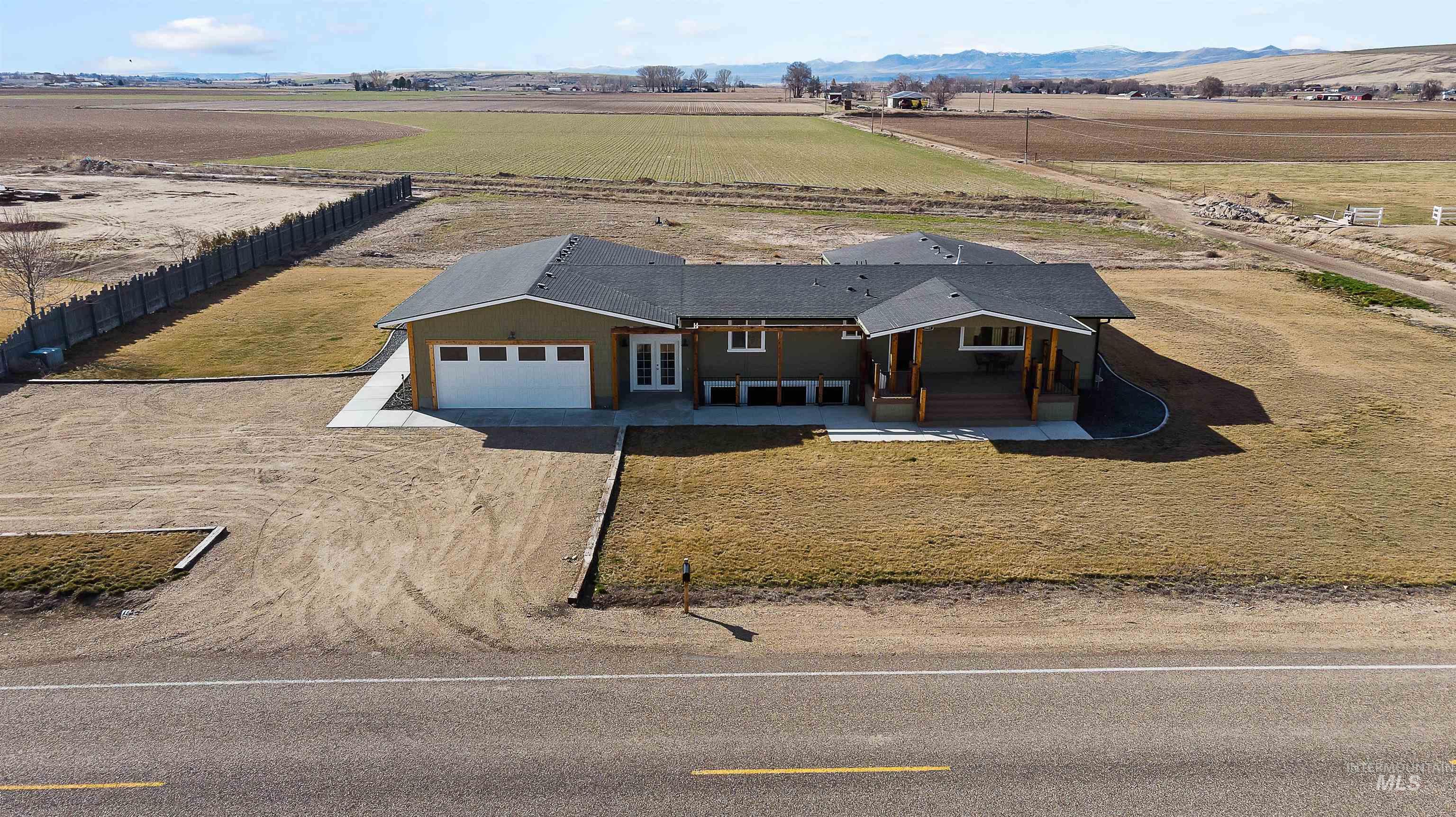 View of front facade with dirt driveway, a patio, an attached garage, and a view of rural / pastoral area