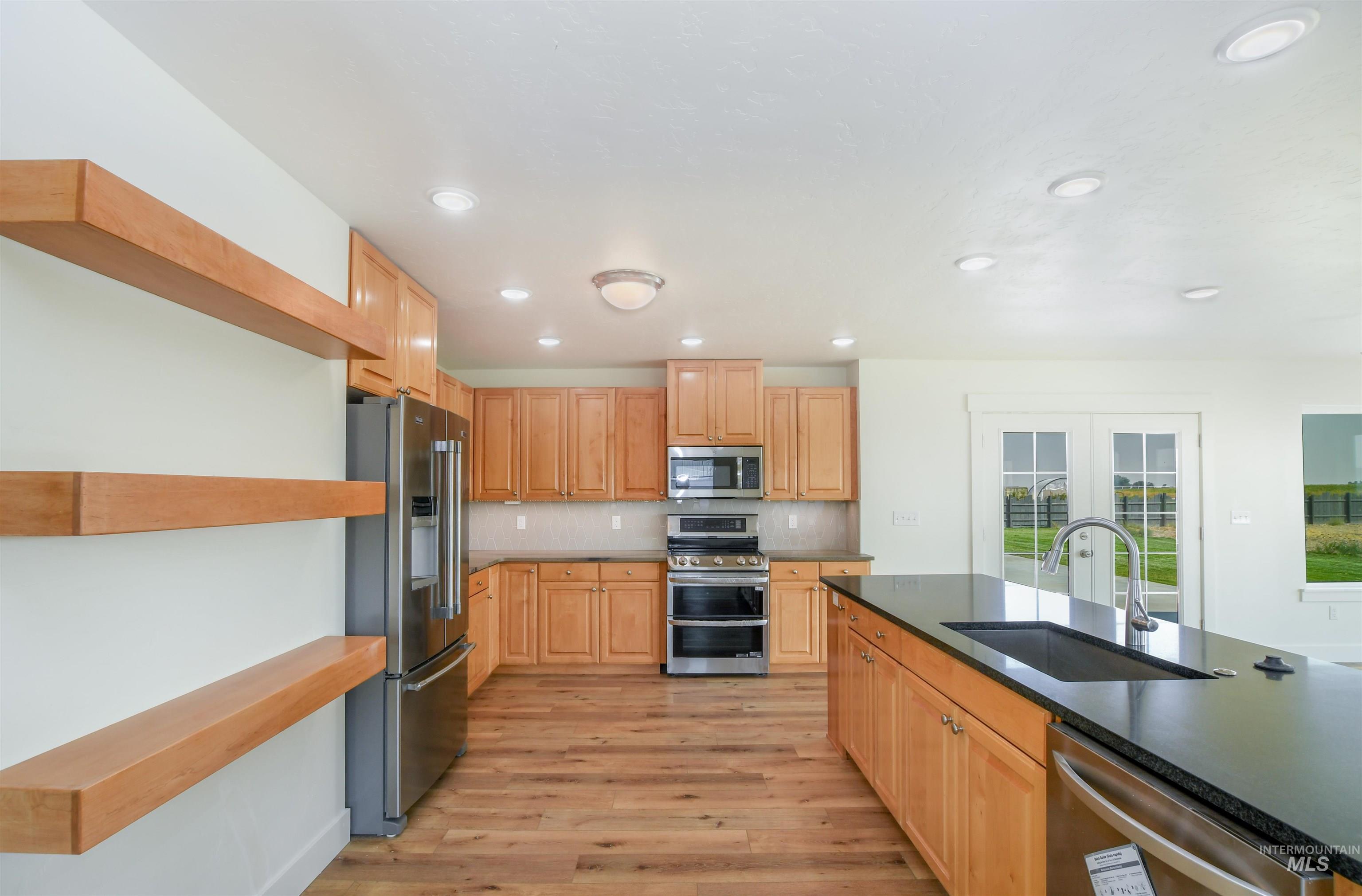 Kitchen featuring french doors, stainless steel appliances, decorative backsplash, light wood-type flooring, and dark stone countertops