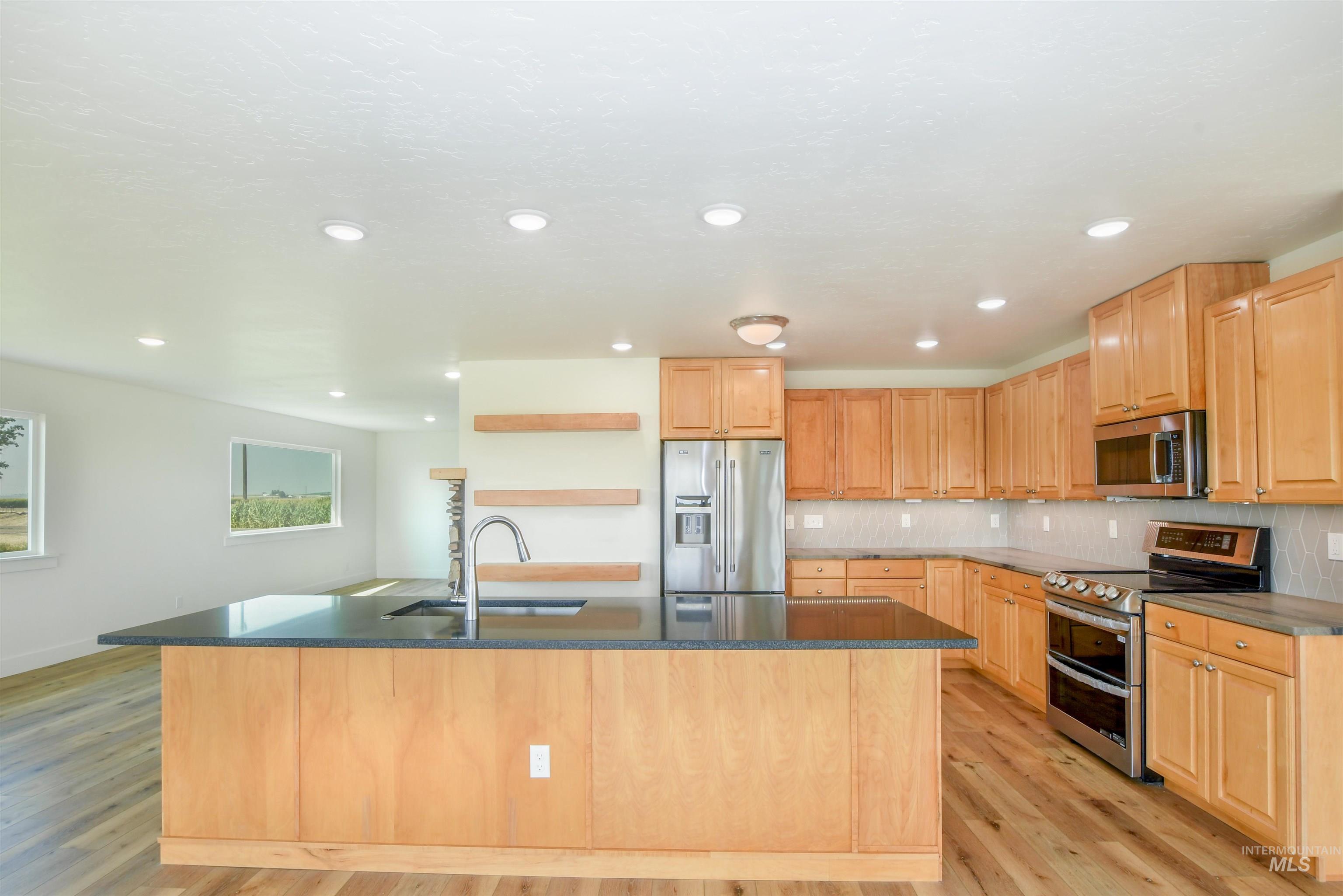 Kitchen with appliances with stainless steel finishes, decorative backsplash, an island with sink, light wood-type flooring, and recessed lighting