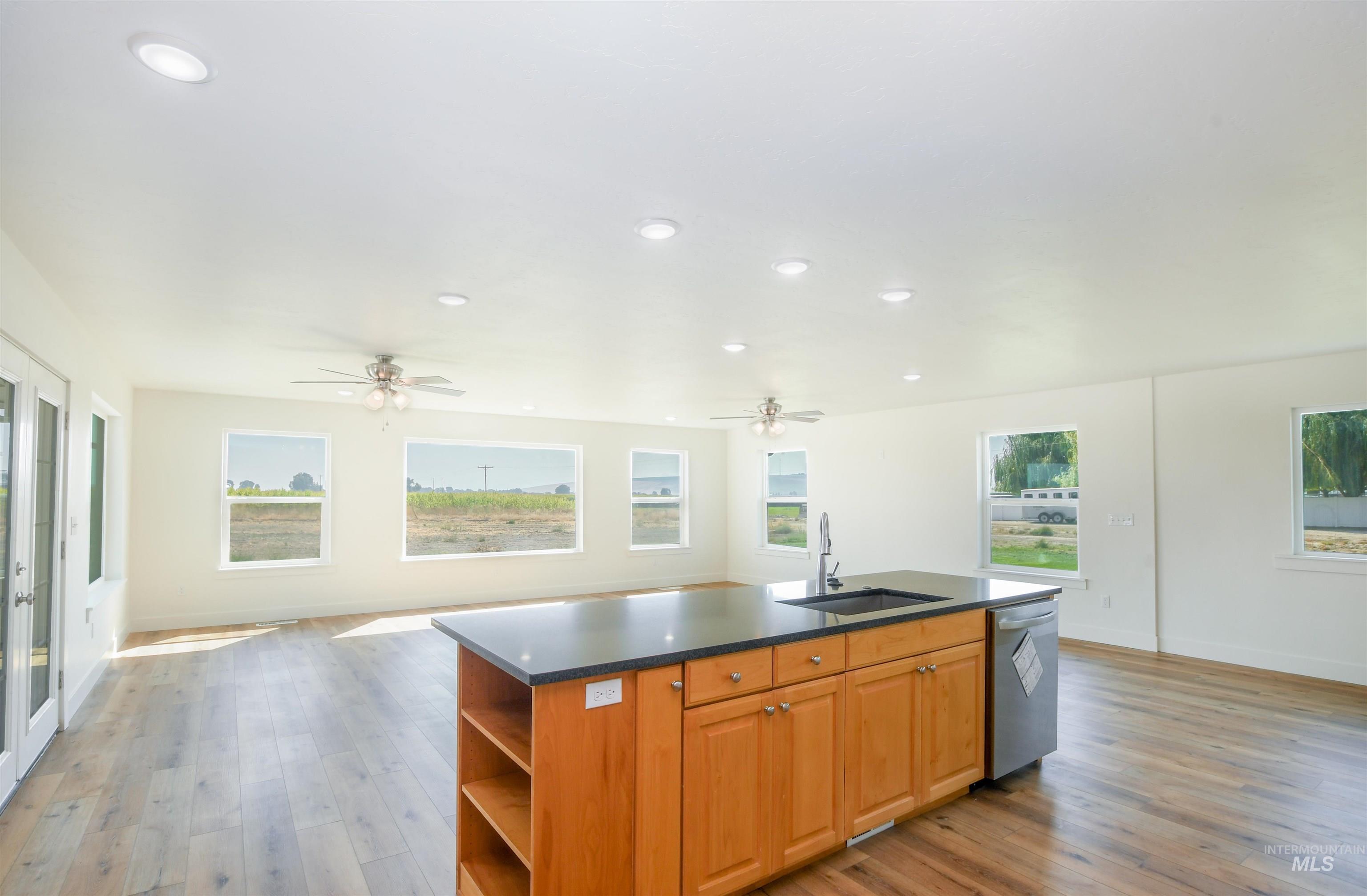 Kitchen featuring open floor plan, a center island with sink, dark countertops, light wood finished floors, and recessed lighting