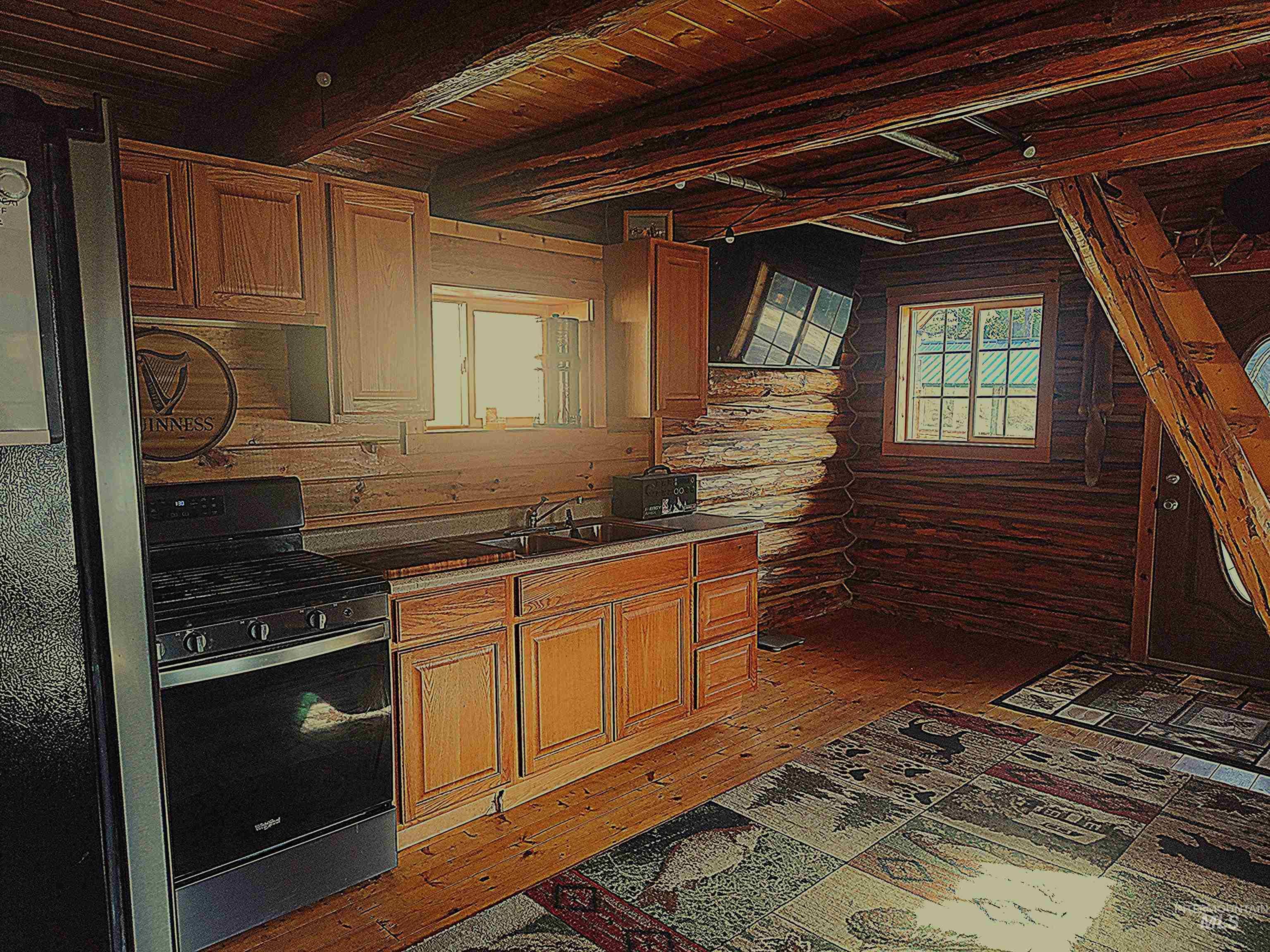 Kitchen with log walls, stainless steel range with gas cooktop, light wood-style floors, brown cabinetry, and a wooden ceiling with exposed beams
