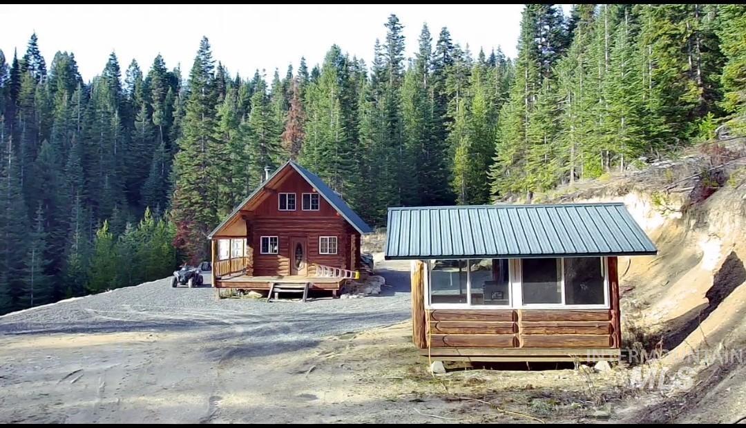 View of front of property featuring a wooden deck, a view of trees, an outdoor structure, and a metal roof