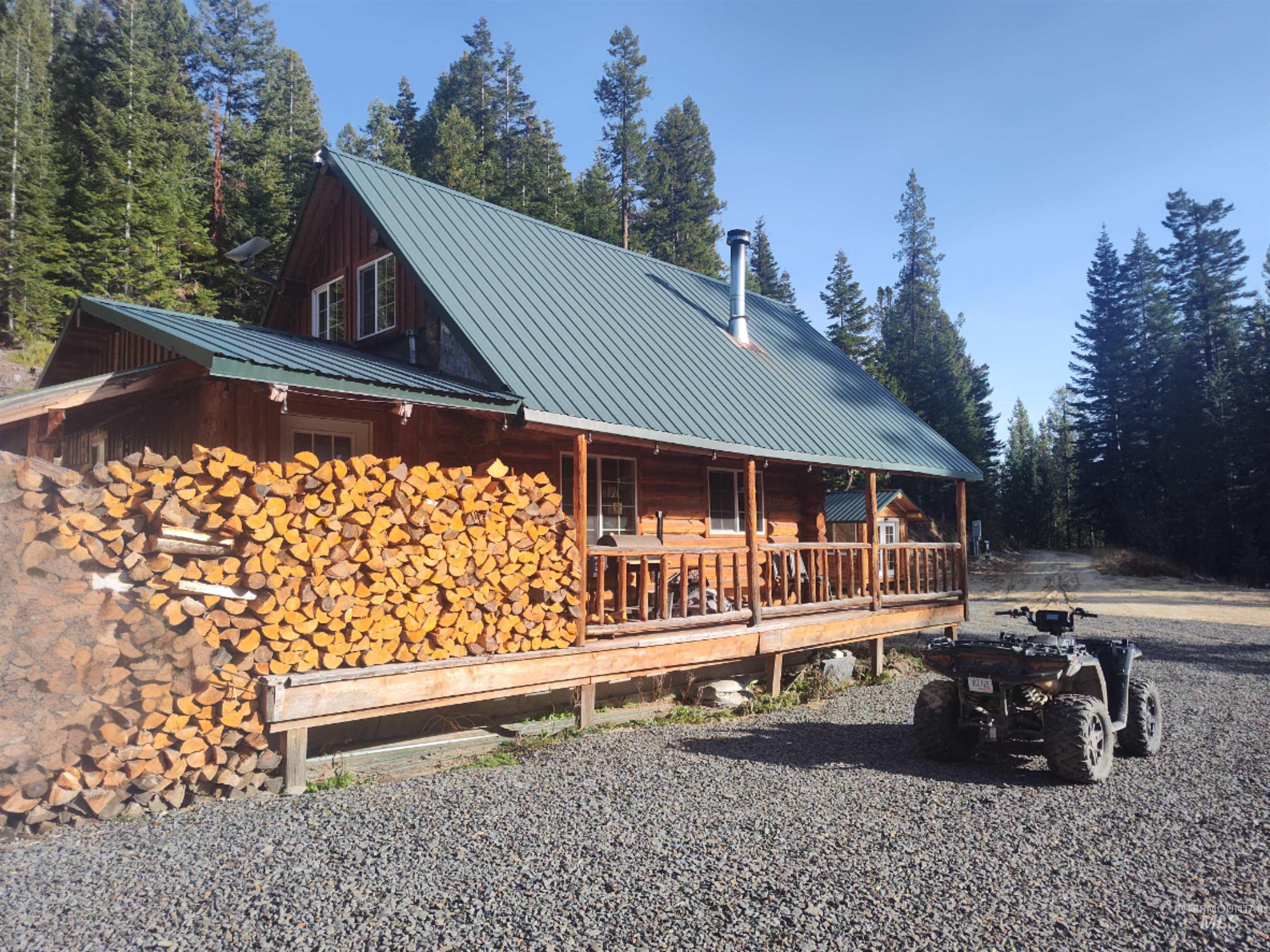 View of property exterior with a porch, a metal roof, a wooded view, and log exterior