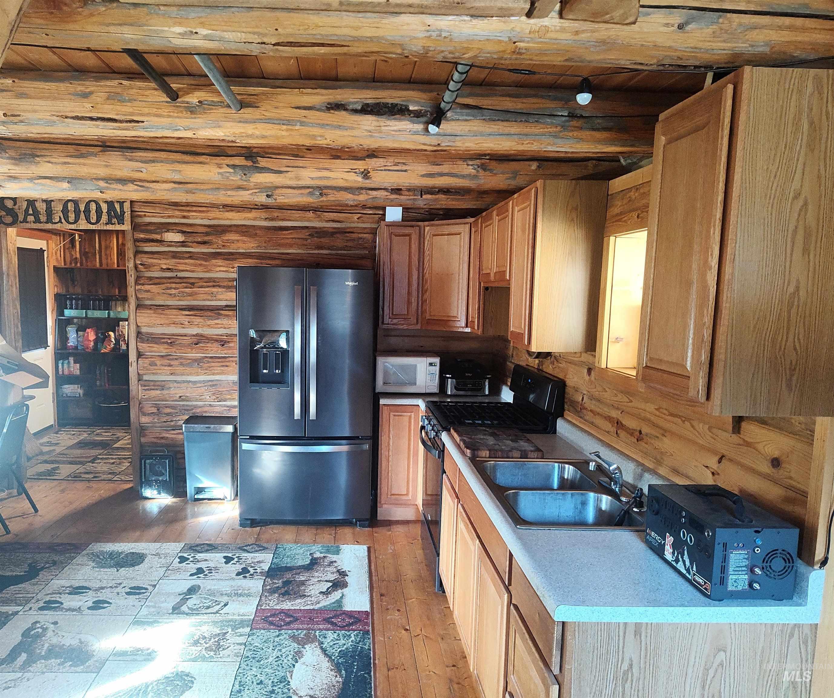 Kitchen with stainless steel fridge with ice dispenser, gas stove, light wood finished floors, a wood ceiling with exposed beams, and white microwave