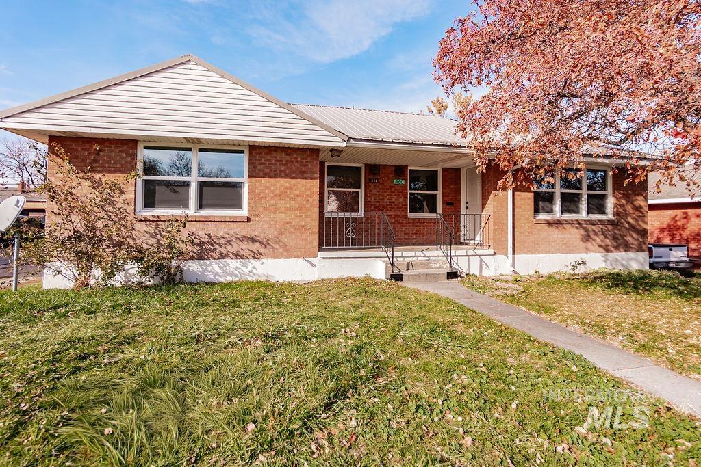Single story home with a front lawn, covered porch, a metal roof, and brick siding
