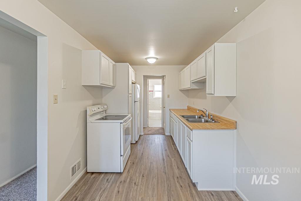 Kitchen with white appliances, light countertops, light wood-style floors, and white cabinetry