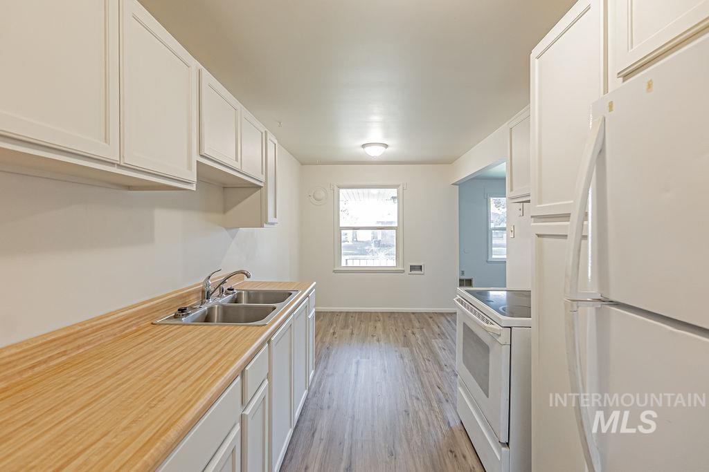 Kitchen featuring white appliances, light countertops, white cabinetry, and light wood-type flooring