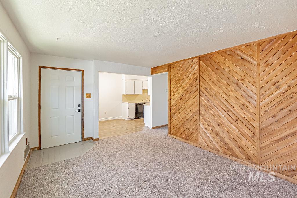 Empty room with light carpet, wooden walls, and a textured ceiling