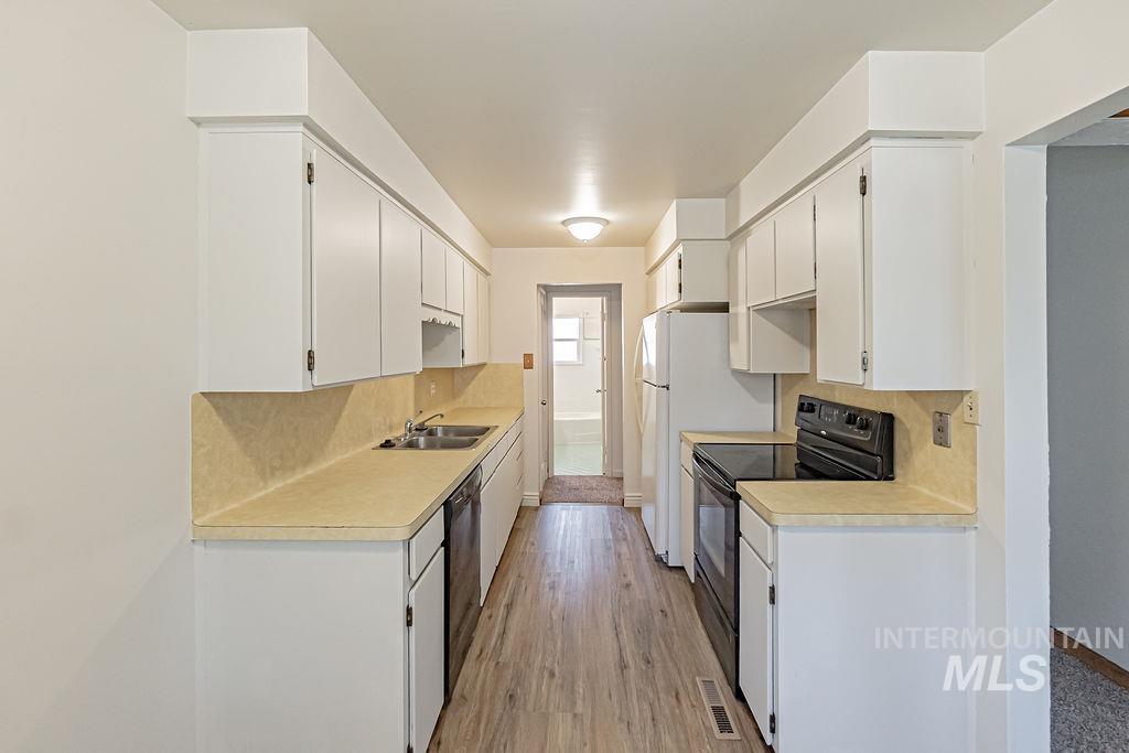Kitchen featuring black appliances, light countertops, tasteful backsplash, light wood-style floors, and white cabinets