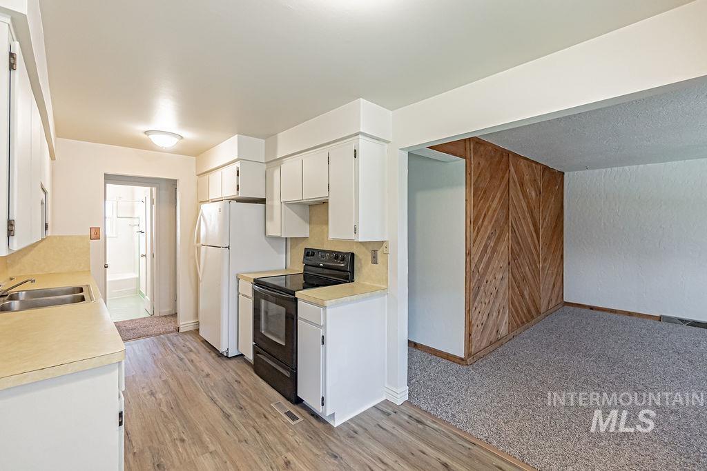Kitchen with black electric range oven, white cabinetry, light countertops, light wood-style flooring, and wooden walls