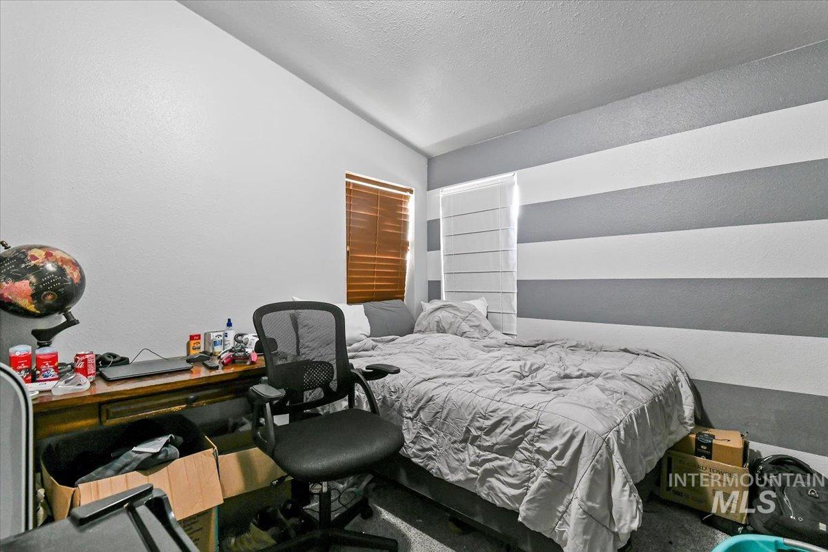 Bedroom with vaulted ceiling, a textured wall, and a textured ceiling