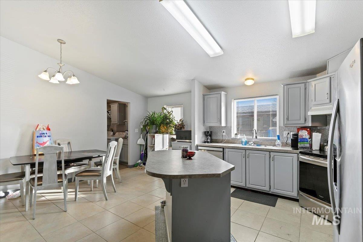 Kitchen with gray cabinetry, tasteful backsplash, light tile patterned floors, appliances with stainless steel finishes, and a textured ceiling