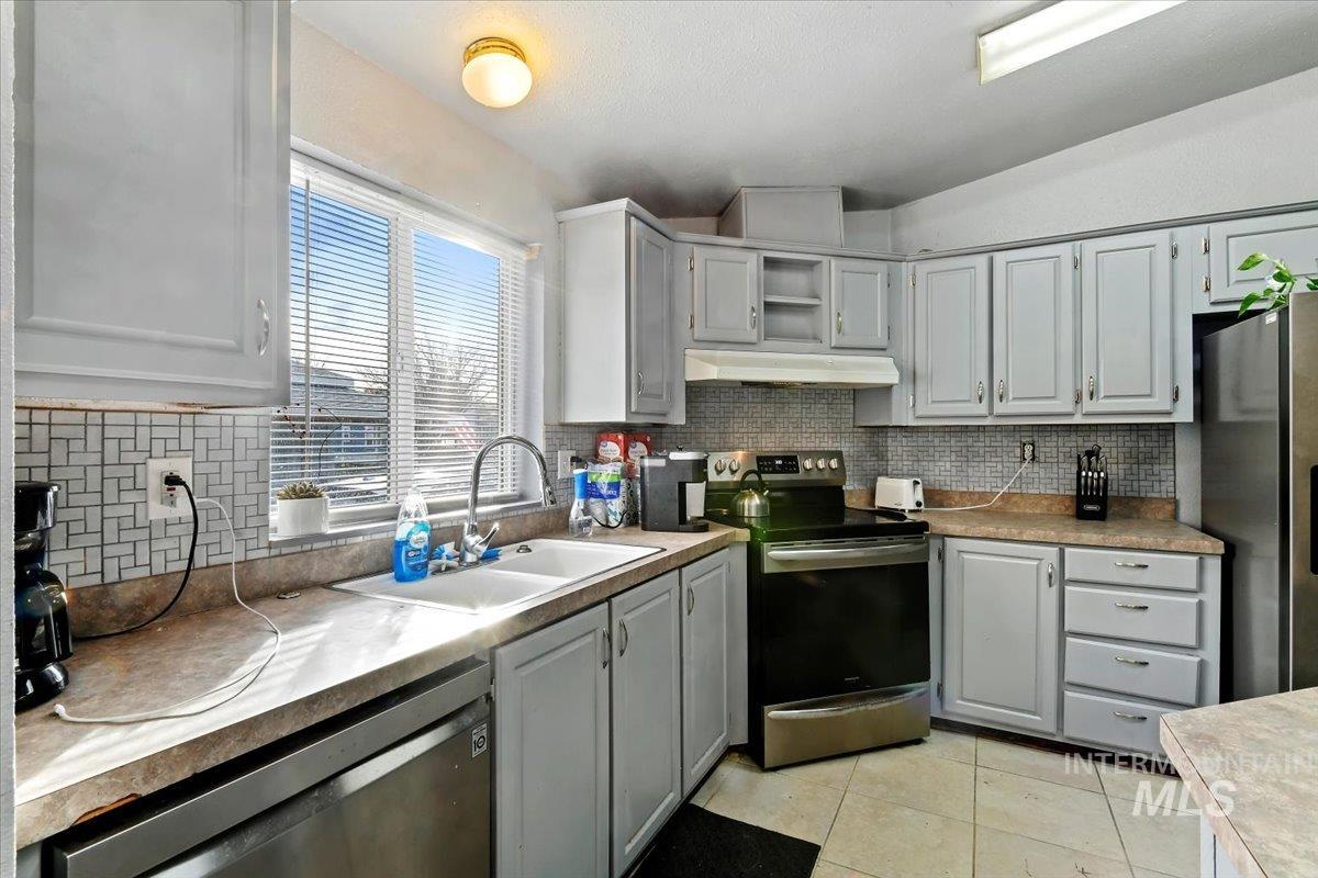 Kitchen with appliances with stainless steel finishes, backsplash, light tile patterned floors, and gray cabinetry