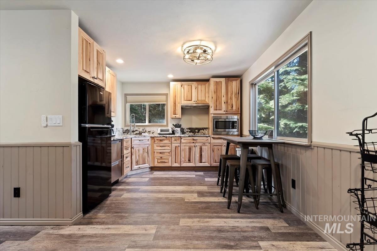 Kitchen with a wainscoted wall, wood walls, light brown cabinetry, appliances with stainless steel finishes, and dark wood-type flooring