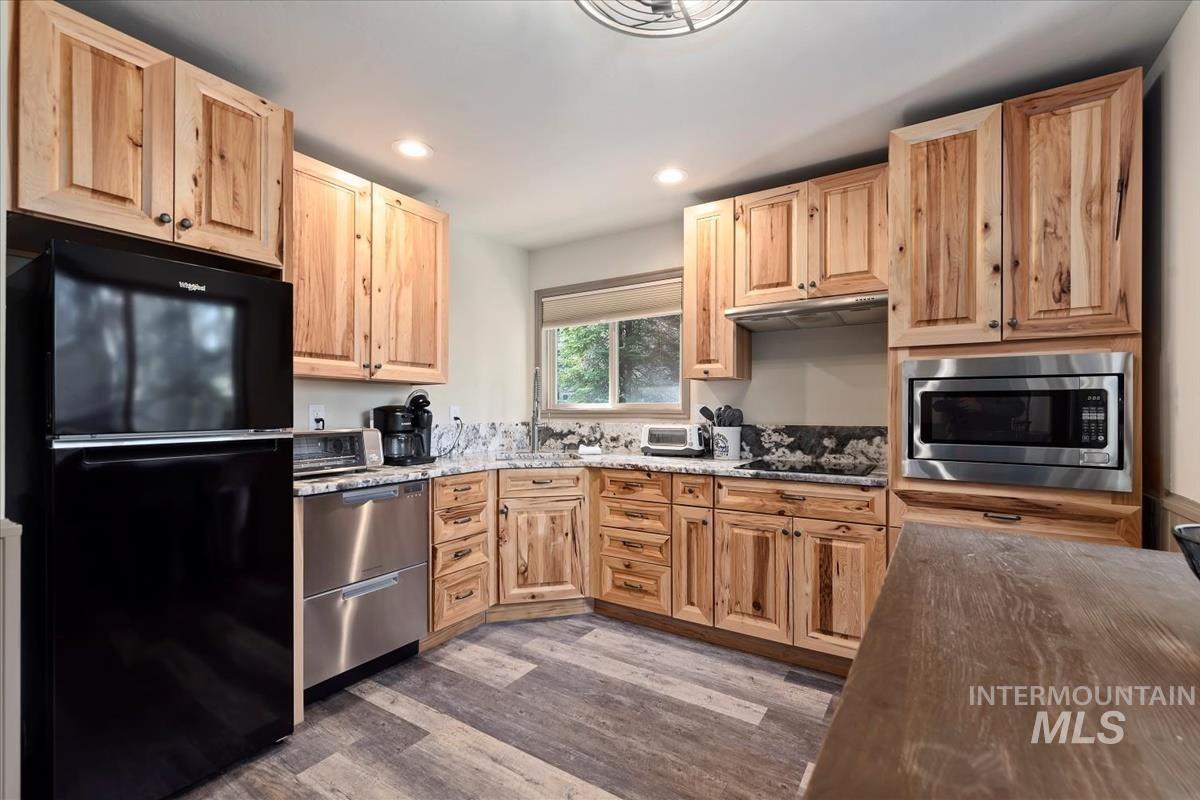 Kitchen featuring black appliances, dark wood-type flooring, dark stone counters, recessed lighting, and light brown cabinetry