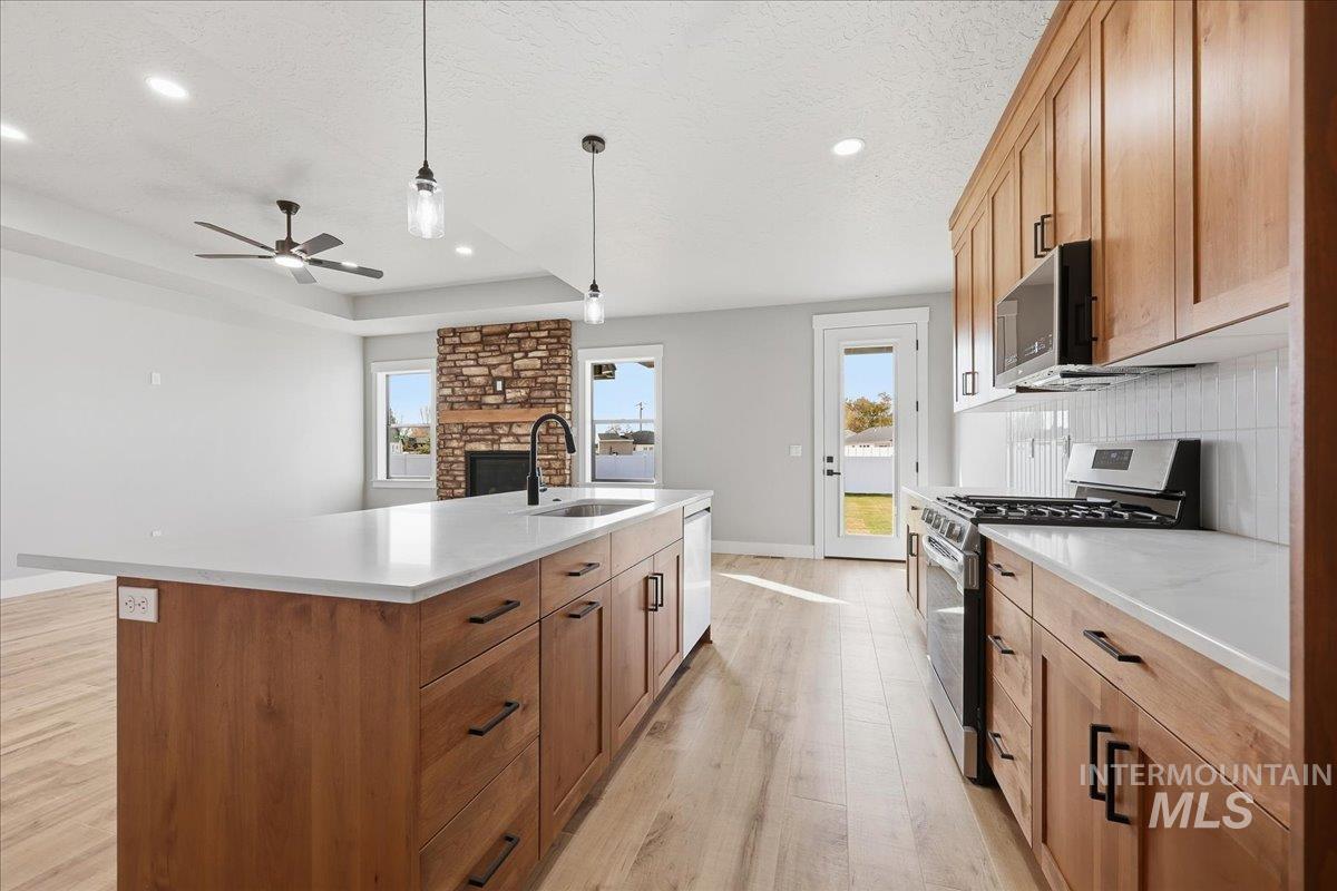 Kitchen with stainless steel appliances, light wood-type flooring, open floor plan, a kitchen island with sink, and light stone countertops