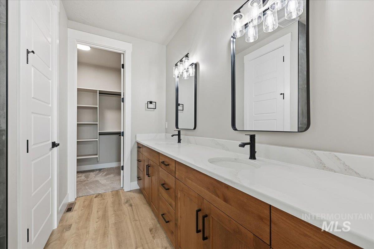 Full bath with light wood finished floors, double vanity, and a walk in closet