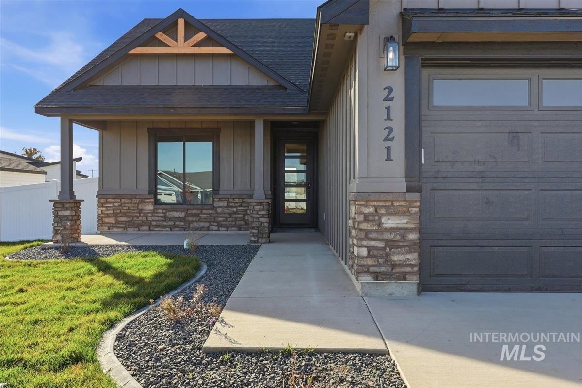 Property entrance featuring stone siding, roof with shingles, board and batten siding, a porch, and a lawn
