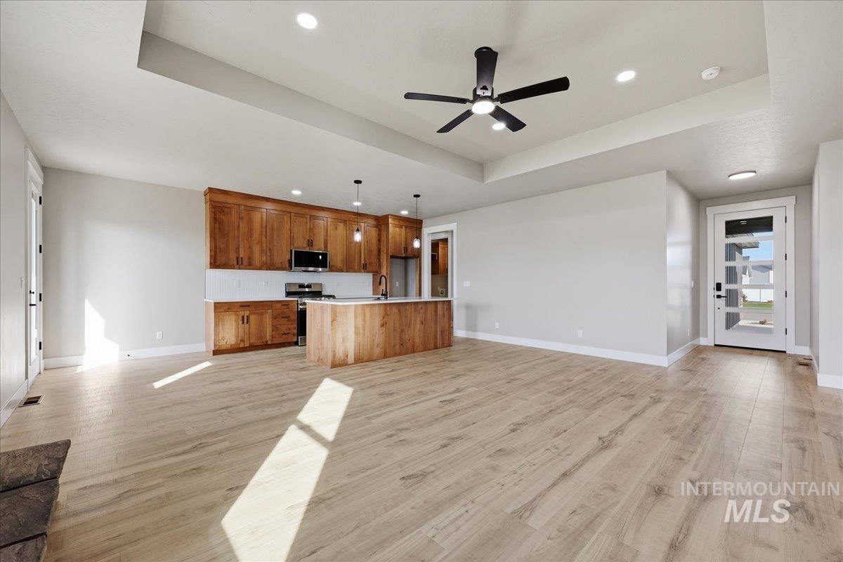Kitchen featuring open floor plan, a tray ceiling, brown cabinetry, light countertops, and light wood-style flooring