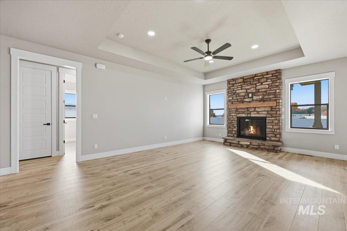 Unfurnished living room featuring a raised ceiling, healthy amount of natural light, light wood-type flooring, a stone fireplace, and recessed lighting