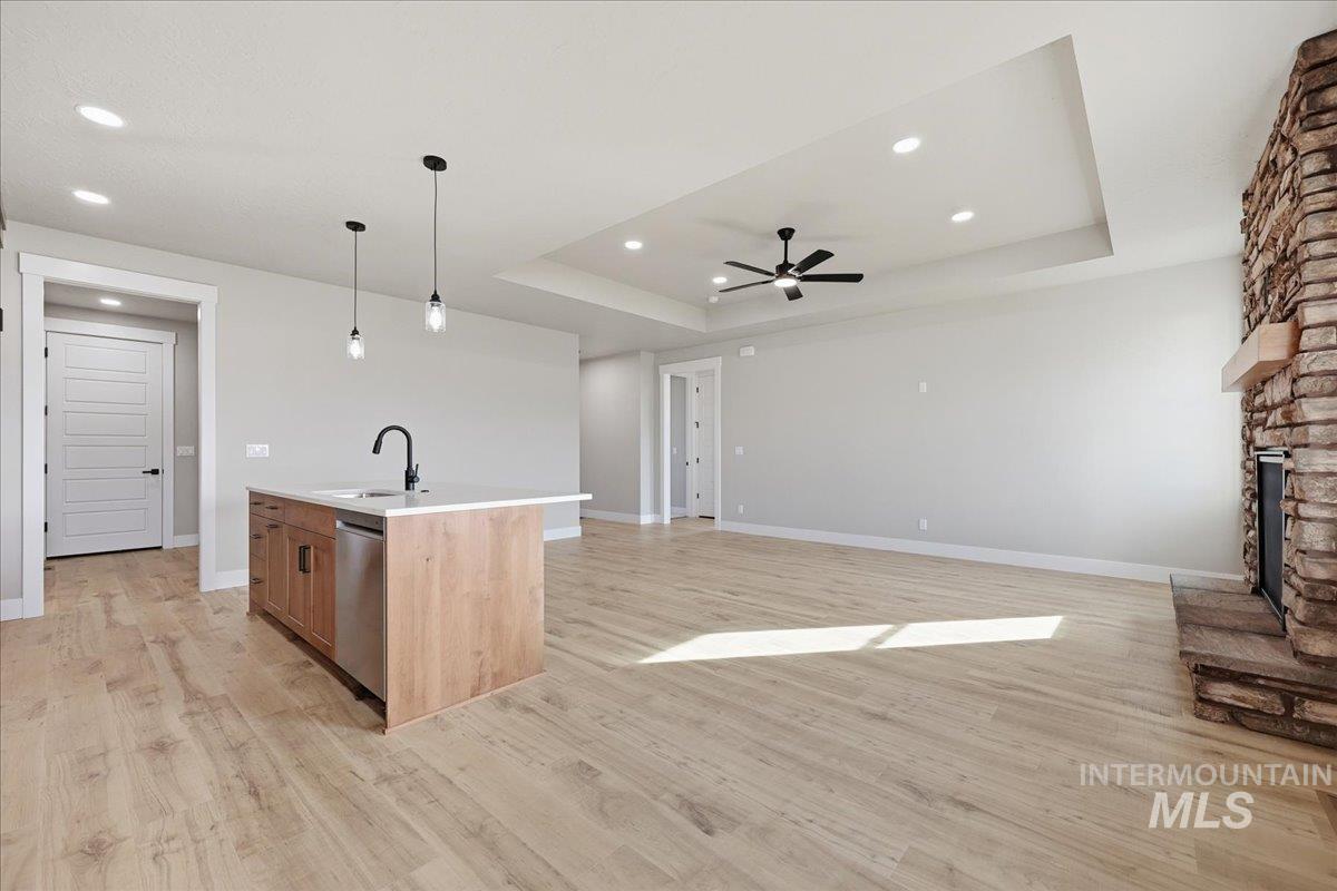 Kitchen with pendant lighting, a kitchen island with sink, a raised ceiling, light wood-style flooring, and open floor plan