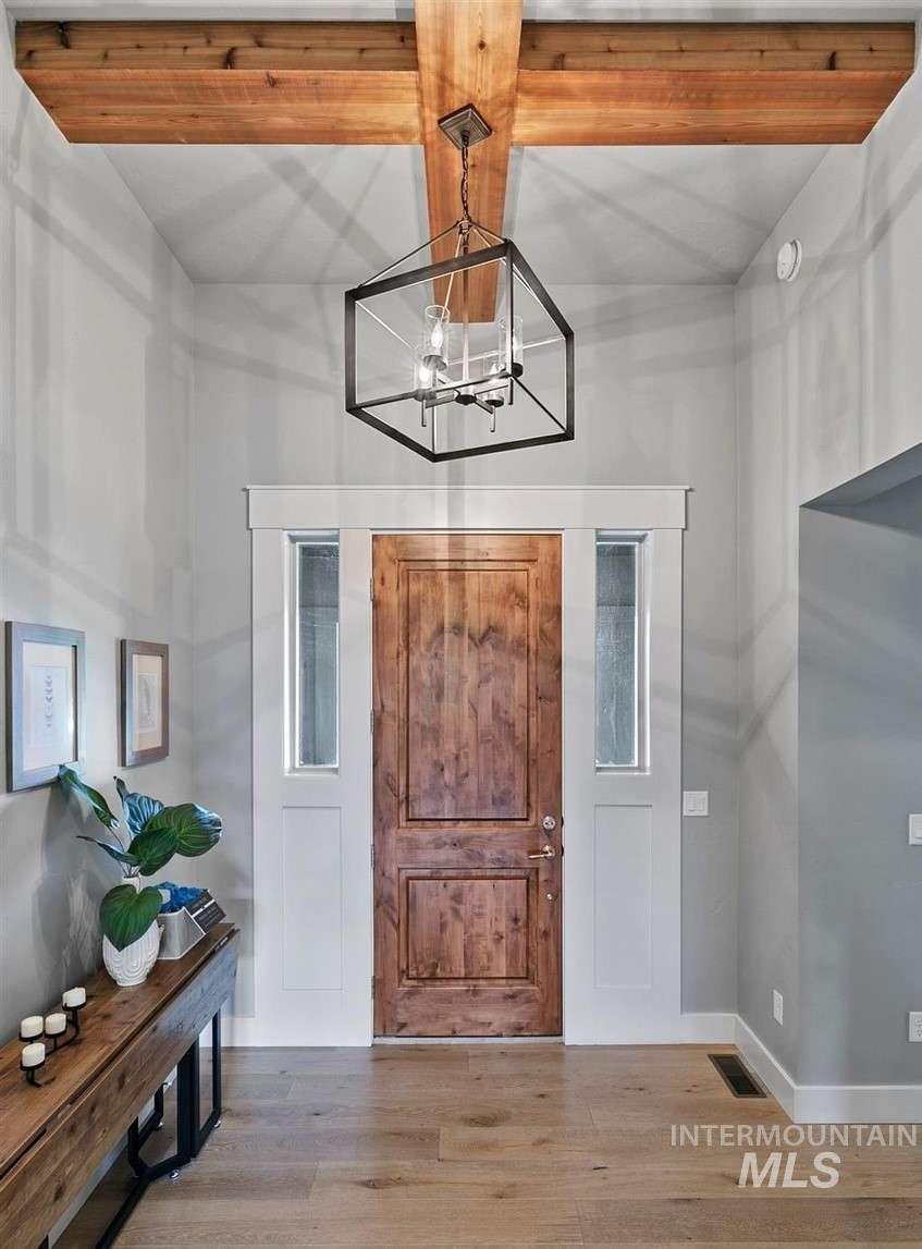 Entryway with wood finished floors, beamed ceiling, and a chandelier