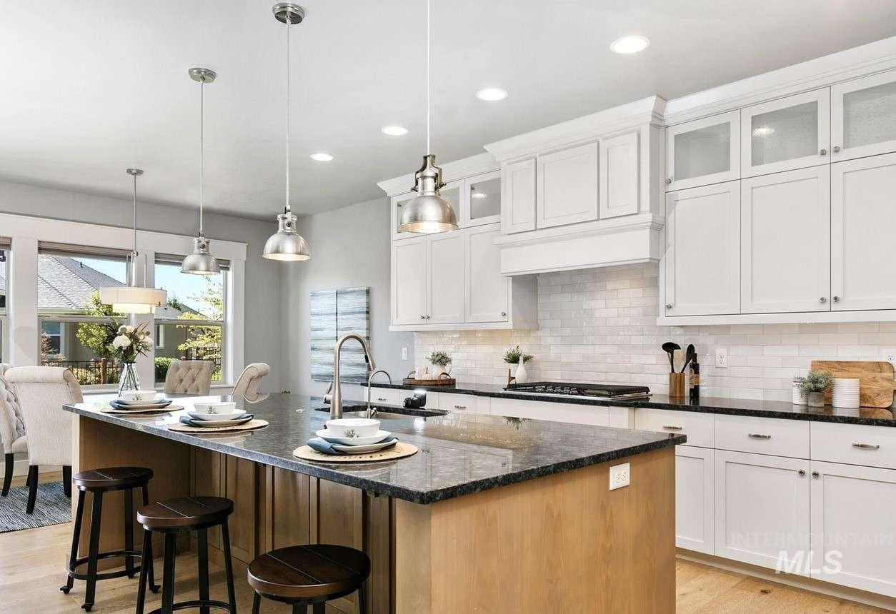 Kitchen featuring dark stone counters, backsplash, a center island with sink, white cabinets, and recessed lighting