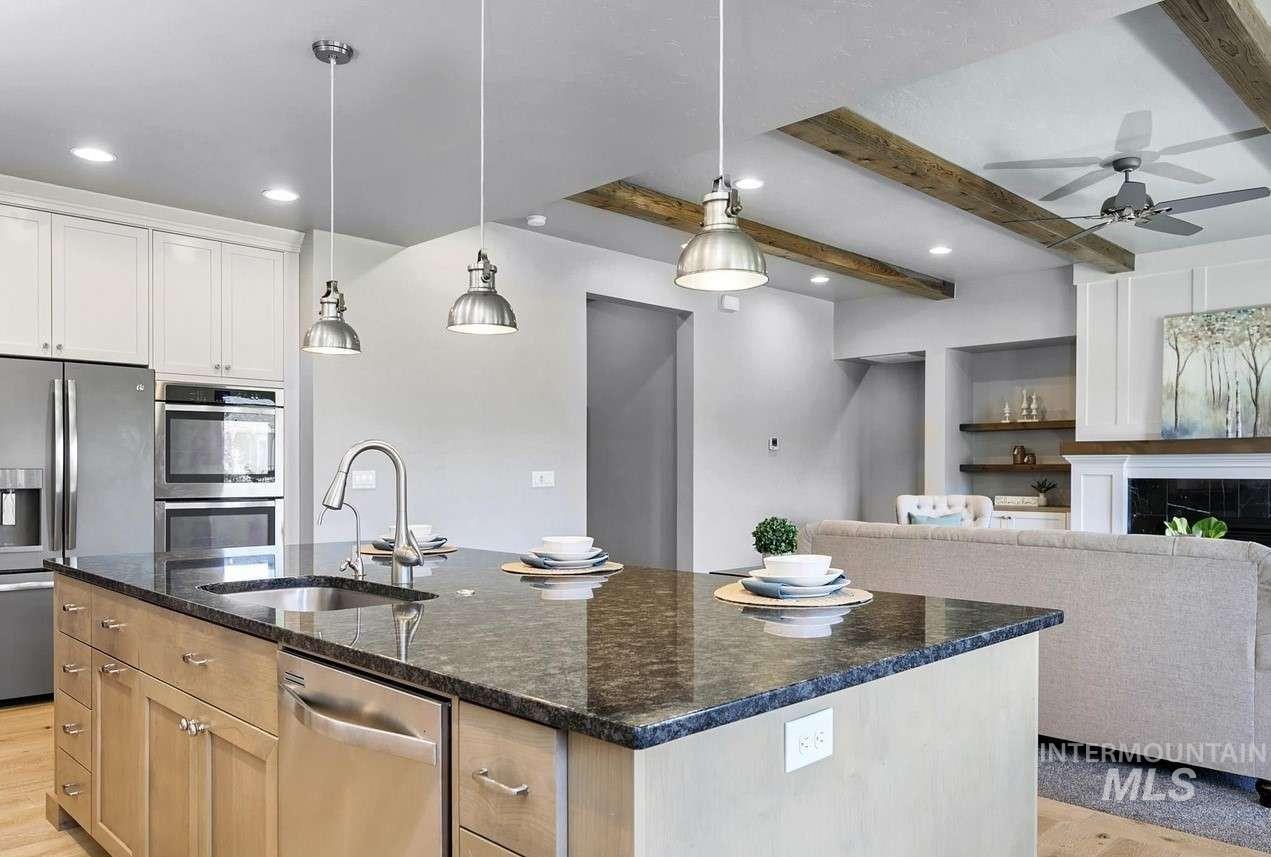 Kitchen with appliances with stainless steel finishes, a center island with sink, dark stone counters, beam ceiling, and decorative light fixtures