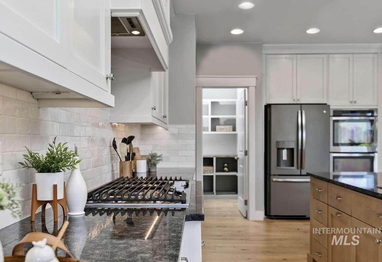 Kitchen featuring appliances with stainless steel finishes, dark stone countertops, exhaust hood, tasteful backsplash, and white cabinetry