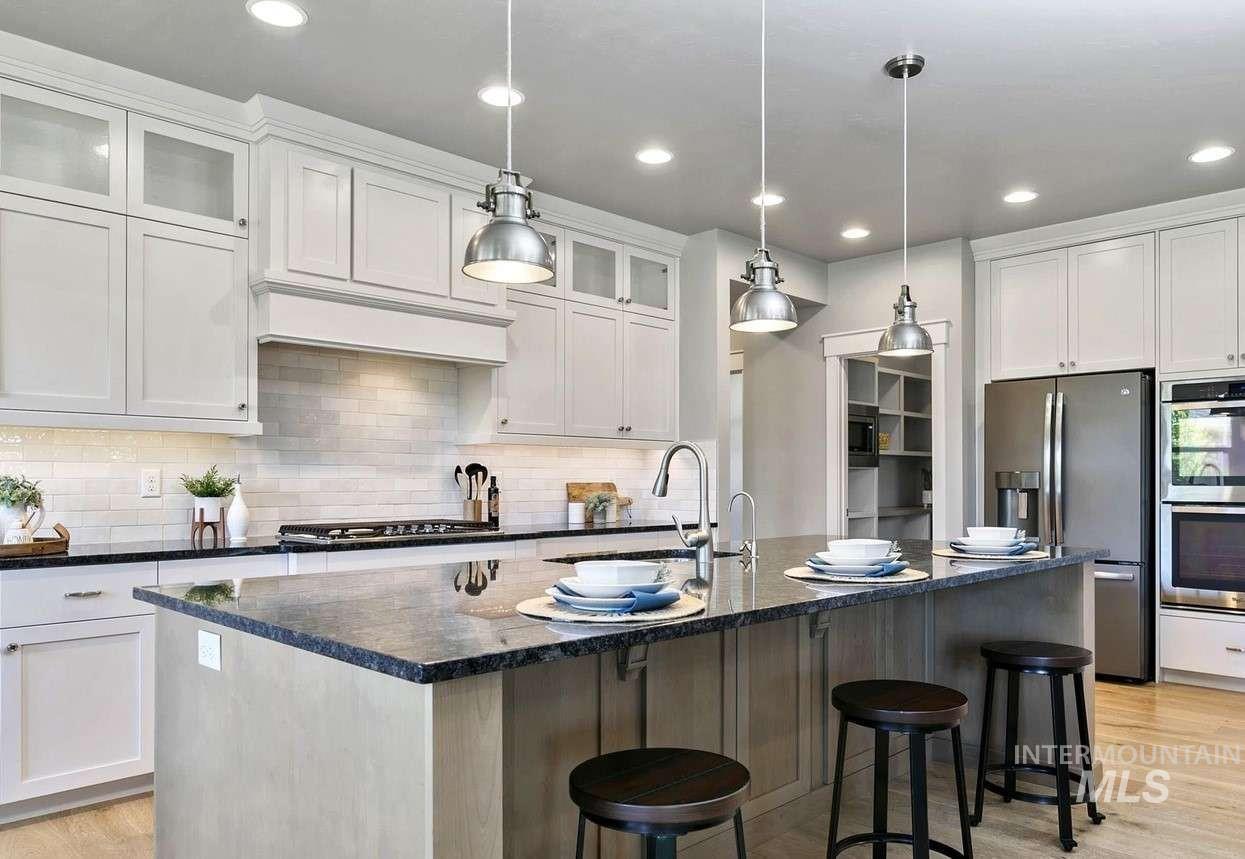 Kitchen with light wood-style floors, dark stone counters, stainless steel appliances, a kitchen bar, and white cabinetry