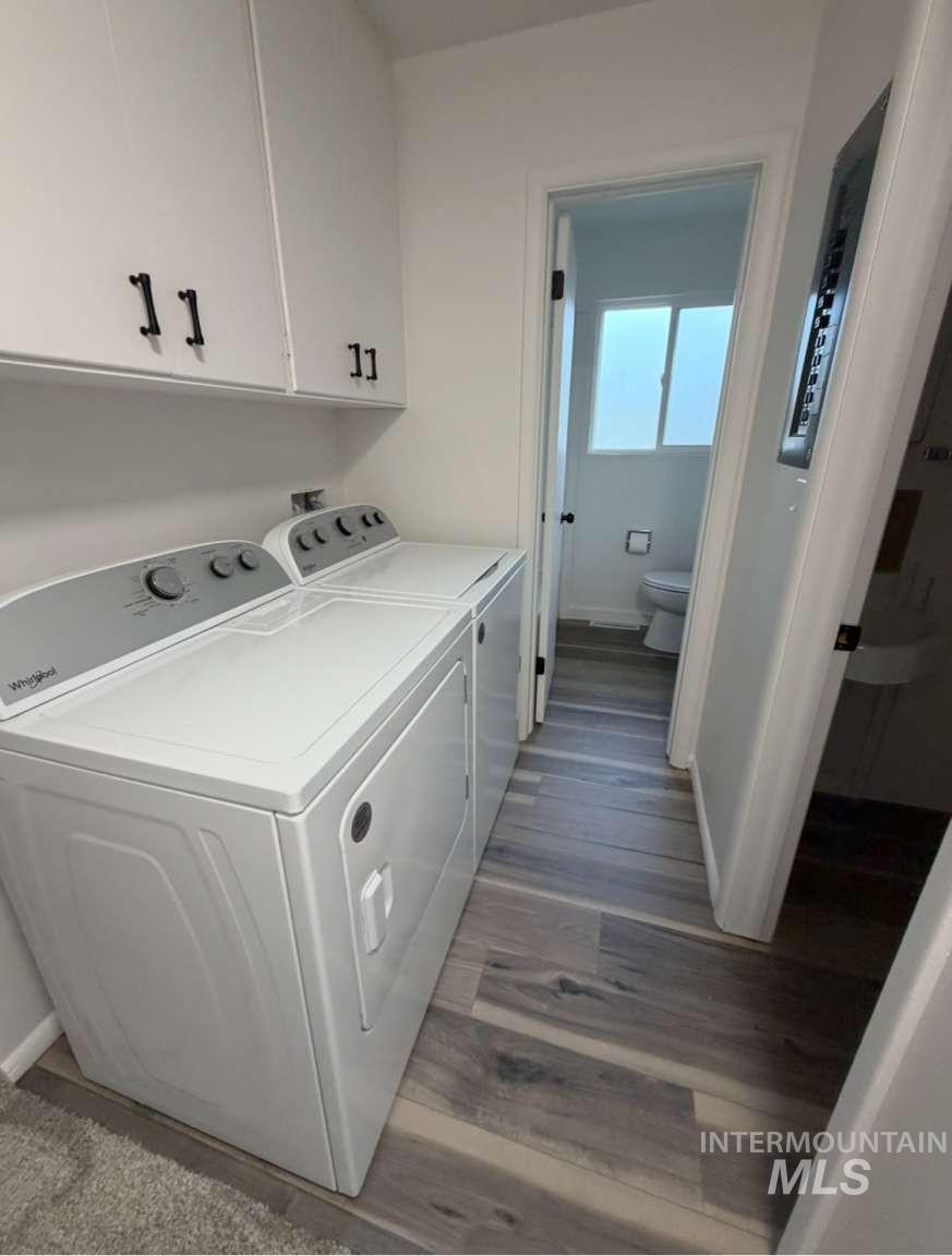 Washroom with cabinet space, light wood-style flooring, washing machine and dryer, and electric panel