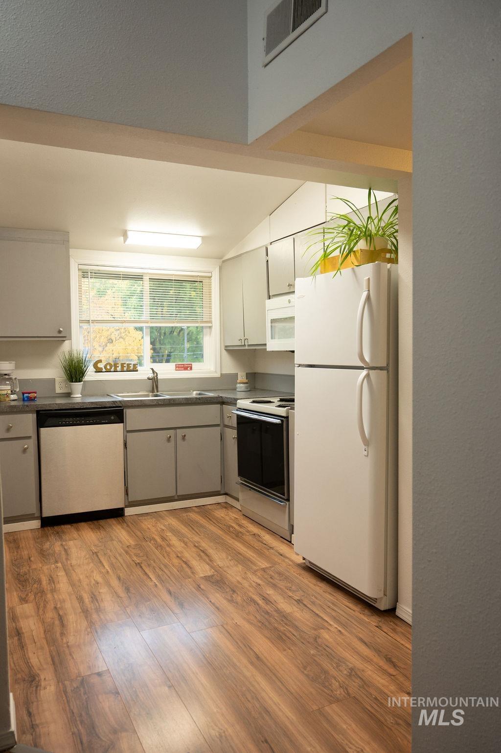 Kitchen with white appliances, light wood-style flooring, gray cabinetry, and dark countertops