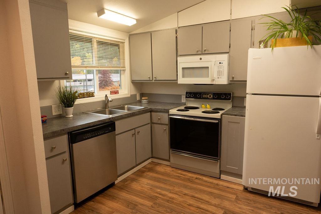Kitchen featuring white appliances, dark countertops, gray cabinets, dark wood finished floors, and vaulted ceiling