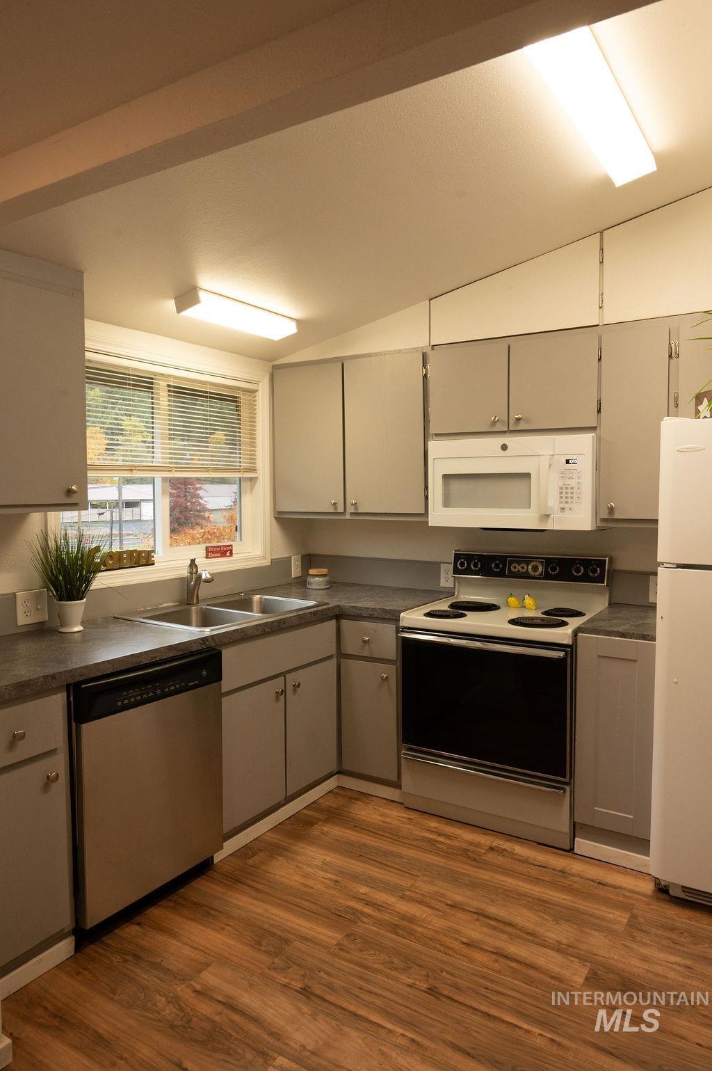 Kitchen featuring dark countertops, white appliances, gray cabinets, dark wood-style flooring, and lofted ceiling