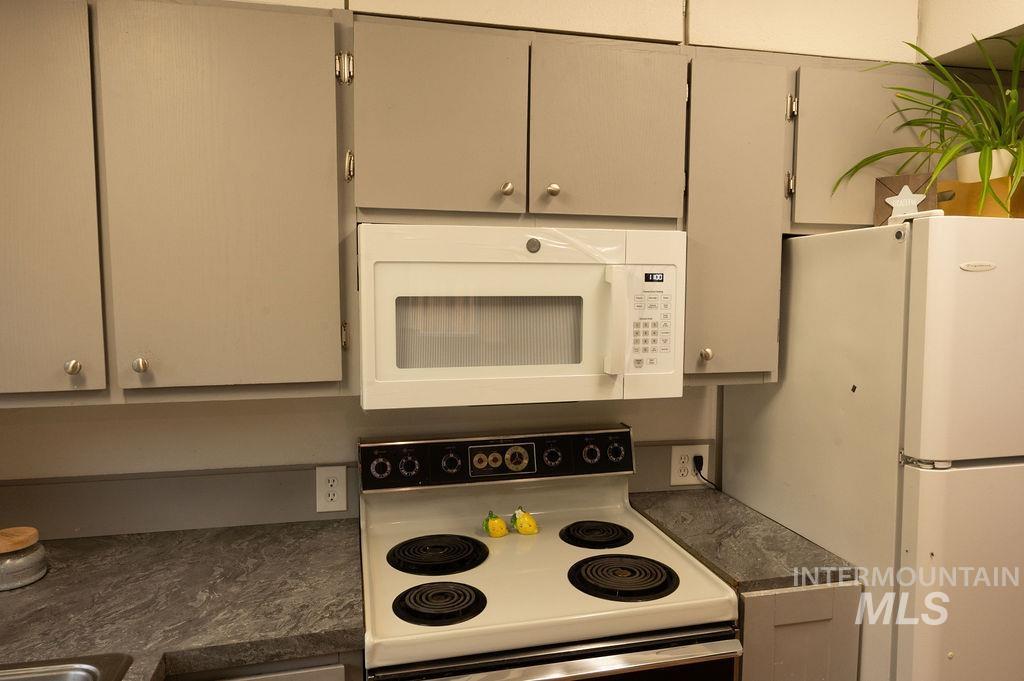 Kitchen with white appliances, dark countertops, and gray cabinets