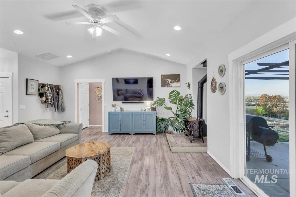 Living room featuring a wood stove, lofted ceiling, light wood-style floors, ceiling fan, and recessed lighting